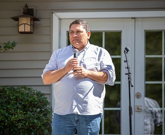 Micheal standing in front of a set of patio doors holding a microphone speaking to an unseen audience