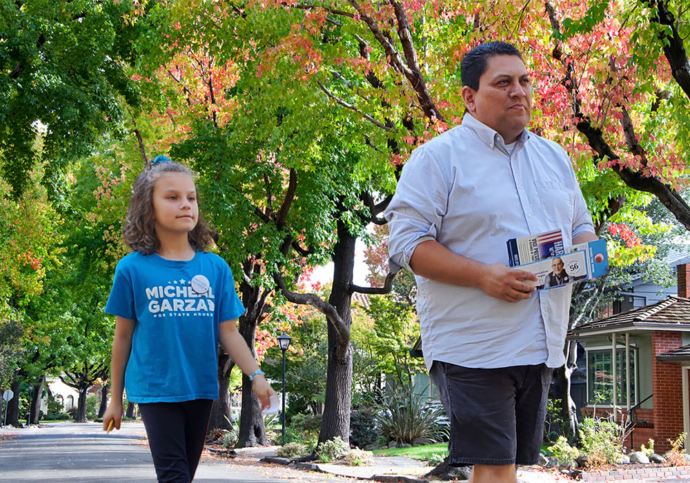 Micheal and his daughter walking in a neighborhood together with trees and houses in the background