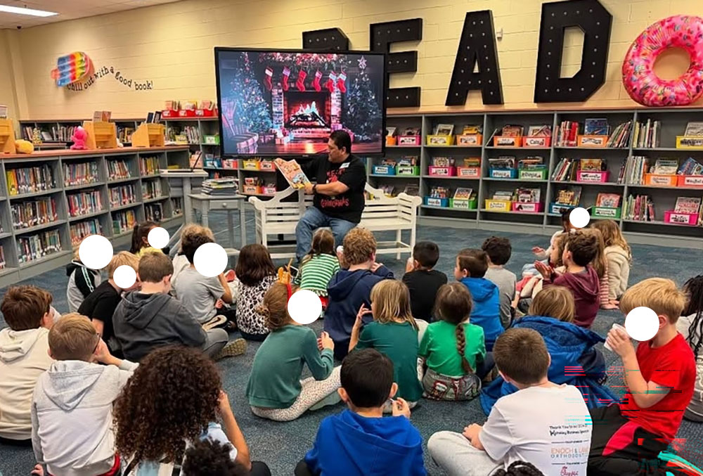 Micheal sitting on a bench reading a book with children seated on the floor listening